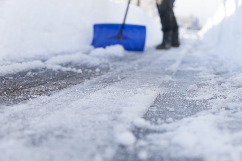 Person shoveling snow and ice off a sidewalk