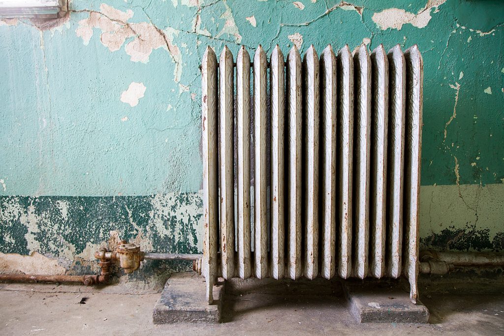 a broken radiator in a dusty poorly maintained room with blue walls. 