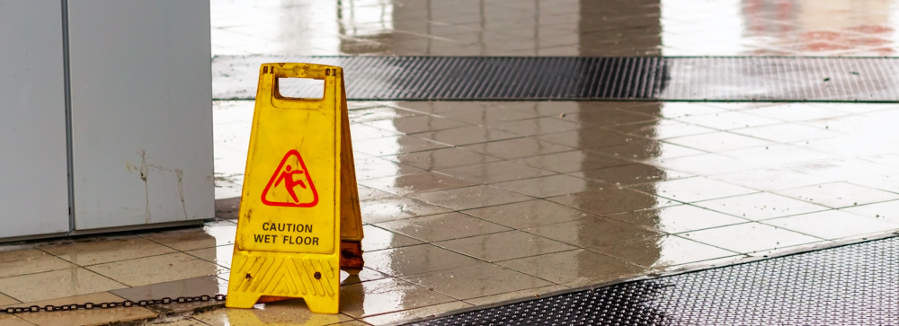 A yellow "Wet Floor" sign stands in the rain slick entry of a building