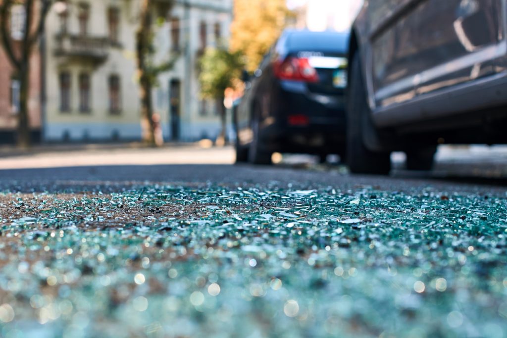 Sharp shards of car glass on the asphalt after a car accident involving two cars.